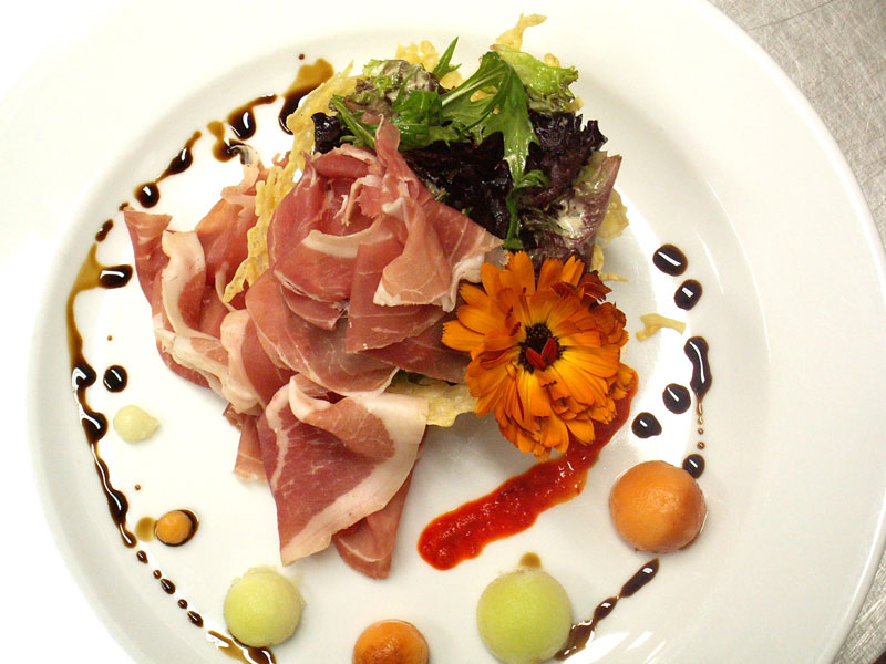 Assiette gastronomique garnie de prosciutto, salade et fleur comestible, préparée par Paul Piché Traiteur