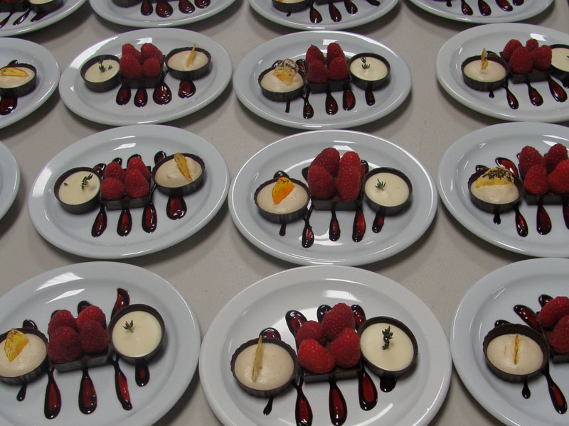 Tartelettes dessert garnies de crème et de framboises, alignées sur un présentoir